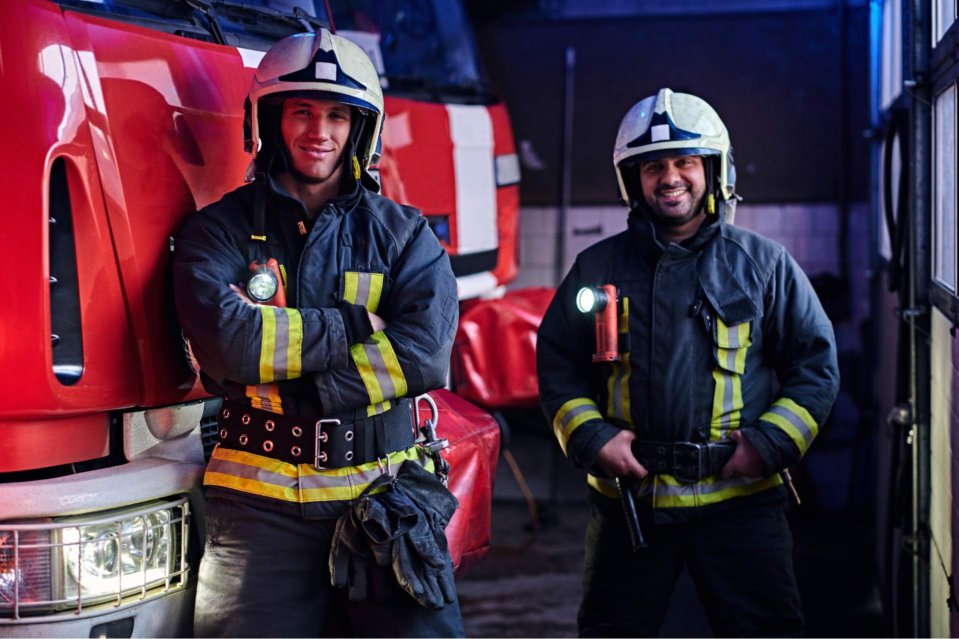 Two firemen posing in front of a firetruck